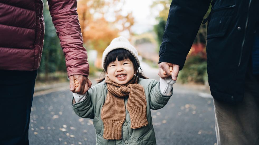 Young girl walking hand in hand with parents